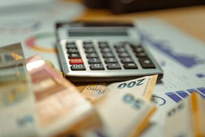 Calcolatrice e banconote in euro appoggiate su fogli con grafici e tabelle finanziarie