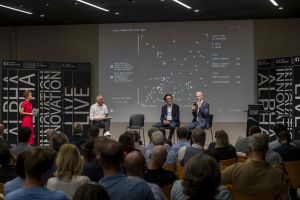 Relatori sul palco della quarta edizione di Alpha Innovation Live al NOI Techpark di Bolzano, con lo schermo che mostra i risultati della survey sui partecipanti